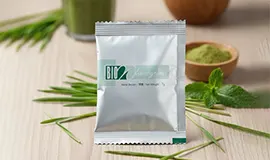 Close-up shot of the silver Bio-Wheatgrass sachet on a wooden surface, highlighting the key ingredients: Wheatgrass Powder and Organic Enzymes.